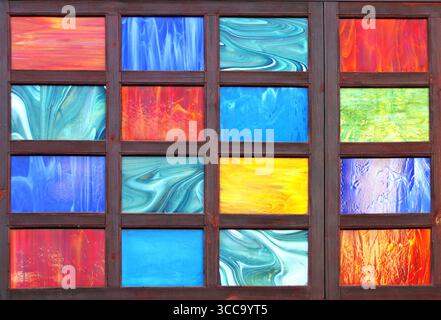 Detail of retro wooden shutter with glass of red, yellow, green and blue colors. Antique wooden shutter, adorned with a glass panel featuring a spectr Stock Photo