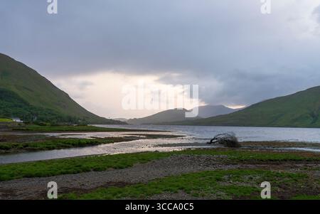 Leenaun waterfront at Killary Fjord, dusk over the Connemara hills, tidal flats and driftwood on the shore, beneath brooding clouds on Ireland’s west. Stock Photo