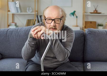 Mature sad man with thick beard feeling sleepy and tired, holding walking stick, focused at camera  Stock Photo