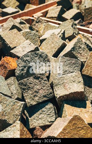 Natural porphyry stone cubes stacked for paving, various earth tones and rough textures in sunlight, construction material background. Selective focus Stock Photo