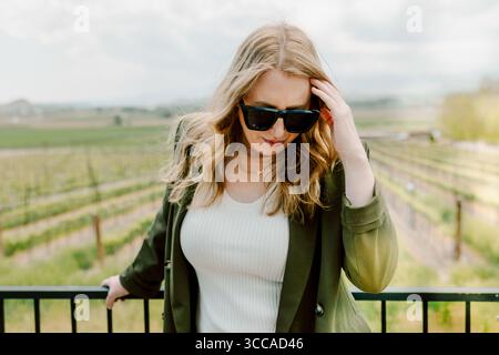 Woman in sunglasses poses confidently at vineyard railing Stock Photo