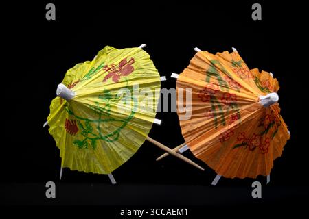 Two colorful cocktail umbrellas with floral decorations crossing on a black background, adding a touch of tropical elegance Stock Photo