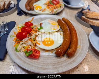 Breakfast for two served in a restaurant, with a focus on a plate of fried eggs, savory sausages, and a healthy salad Stock Photo
