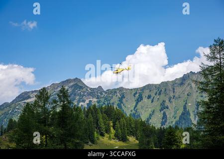 Yellow mountain rescue helicopter of emergency medical service flying over Austrian Alps. Safety and emergency support in wilderness Stock Photo
