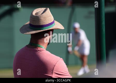Man wearing  a straw hat sitting at one of the outside courts watching a player at the 2025 Wimbledon Championships, London,England,UK. Stock Photo