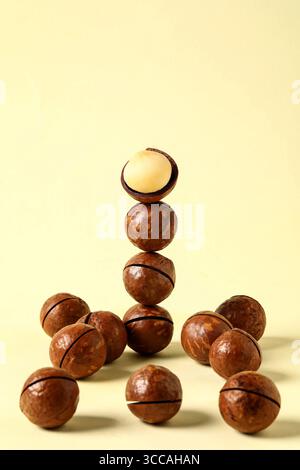 Stacked Macadamia Nuts with One Open Nut on Top,  Studio Shot on Pale Yellow Background, Macadamia nuts in the form of a pyramid Stock Photo