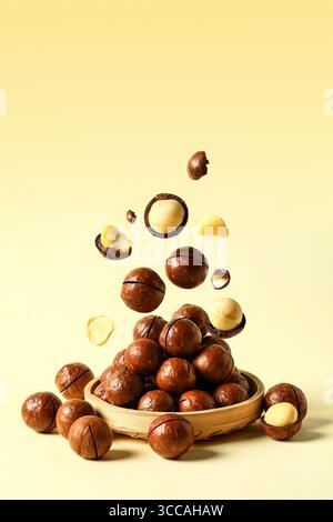 Delicious Macadamia Nuts in a Wooden Bowl with Some Falling - Healthy Snack Food Concept, Falling chestnuts in a basket on a white background. Stock Photo