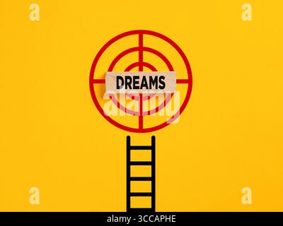 Realize a dream concept. Ladder leading to a target with a wooden block with the word dreams in the center on a yellow background Stock Photo