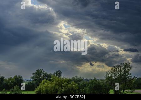 Thick, grey clouds cover the sky over a green landscape. The sun occasionally breaks through the clouds and creates a dramatic contrast Stock Photo