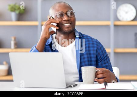 Coffee break. Happy african american employee talking on cellphone and holding cup with hot drink Stock Photo
