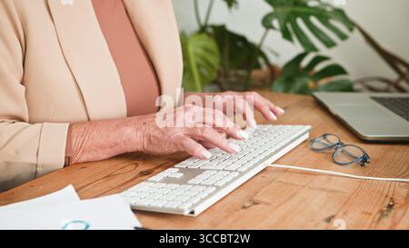 Older Woman Typing on Keyboard at Desk in Professional Business Environment Stock Photo