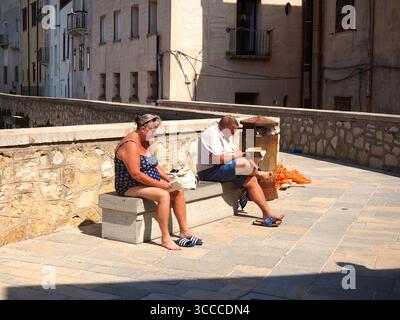 Elderly couple in swimsuits reading books on stone bench in historic old town Trapani Sicily Italy on bright summer day with Mediterranean backdrop Stock Photo