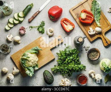 Various healthy vegetables ingredients on kitchen desk background with knife, herbs, spices and cutting boards. Top view. Vegan food Stock Photo