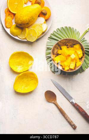 Empty mango peels and coconut bowl with mango cubes on white background with knife and spoon, top view.  Mango preparation Stock Photo
