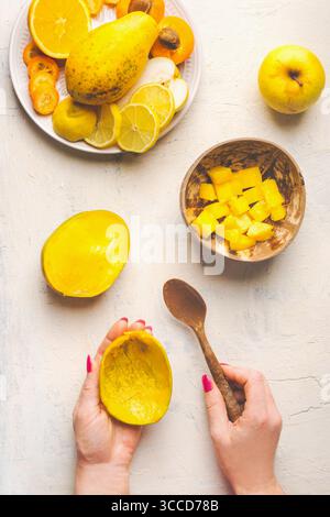 Mango preparation step by step. Female hands holding empty mango peel and spoon on white background with mango cubes in coconut bowl and fruits plate, Stock Photo