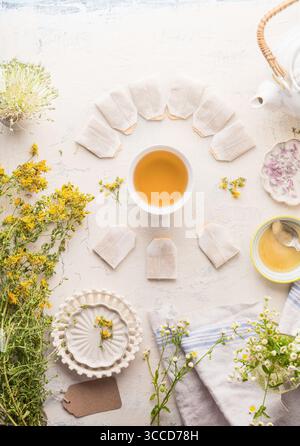Cup with frame of tea bags of herbal tea on white table background, top view. Herbal tea setting with teapot , honey and fresh medical herbs and flowe Stock Photo