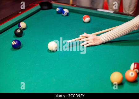 Woman playing billiards aiming the white ball with the cue on a green pool table during a game Stock Photo