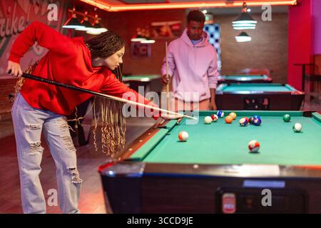 Two young adults playing pool in a colorful, neon lit billiard room, enjoying a friendly game Stock Photo