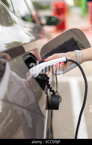 Close up of woman's hand inserting power cable supply plugged into electric car charging, green energy concept Stock Photo