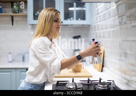 Young woman preparing coffee in a sleek, modern kitchen, using a classic italian moka pot, enjoying the rich aroma of her morning brew Stock Photo