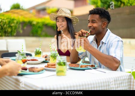 Young people having lunch together, drinking lemonade and eating barbecue outdoors in the garden Stock Photo