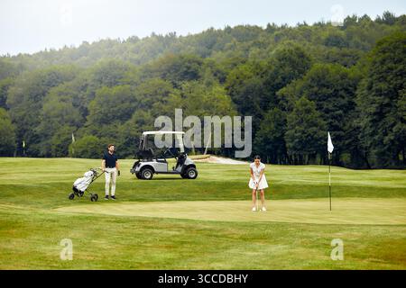 A couple is enjoying quality time together on the golf course, sharing laughter and exchanging their golf equipment, which beautifully highlights the Stock Photo