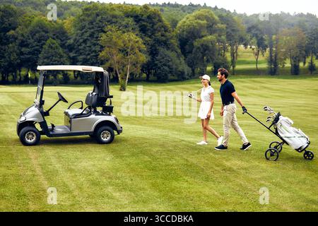 A couple takes a leisurely stroll on a beautifully maintained golf course, enjoying their time together with a golf cart and all the necessary equipme Stock Photo