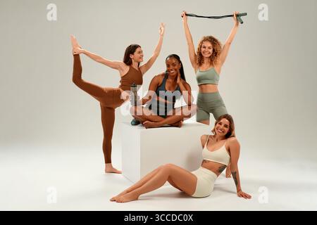 Four diverse young women, including African American and Caucasian, in colorful activewear, smiling and posing together, expressing fitness, body posi Stock Photo