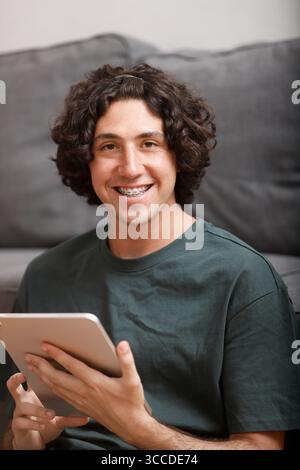 Happy young man with braces using digital tablet, enjoying online activity or working remotely Stock Photo