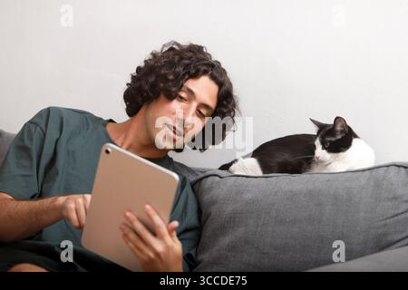 Young man using digital tablet with cat relaxing on sofa Stock Photo