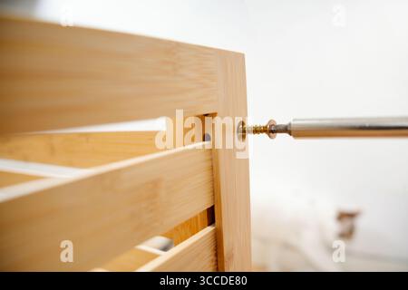 Close-up of screwdriver tightening screw into wooden furniture during assembly process Stock Photo