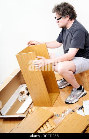 Man assembling new furniture, while his cat watches him from inside the box Stock Photo