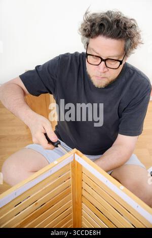 Concentrated man assembling wooden furniture using screwdriver at home Stock Photo