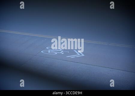 White painted bicycle symbol and direction arrow on a dark asphalt bike path or lane guiding cyclists, promoting urban commuting and active lifestyle Stock Photo
