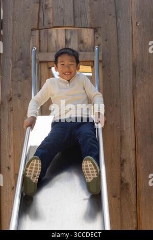 Happy boy having fun sliding down a metal slide at the playground Stock Photo