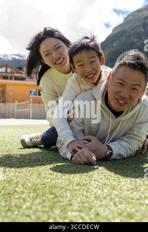 Happy asian family is lying and playing together on a green synthetic grass field in the mountains Stock Photo