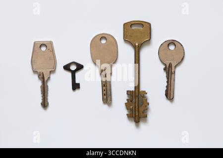 Five metal keys of different shapes and sizes old and arranged in a row on a white background Stock Photo