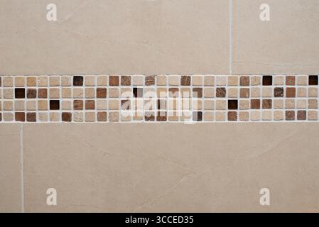 Mosaic tiles in earthy browns and creams create a decorative border on a beige tiled wall, adding stylish touch to interior wall designs for bathrooms Stock Photo