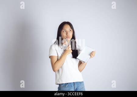 Young asian woman is shown contemplating while holding a pen to her lips and a notebook in her other hand. Stock Photo