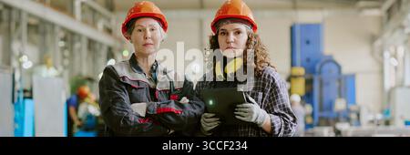 Header with Two Caucasian Female Factory Workers Standing Confidently in Industrial Workshop Stock Photo