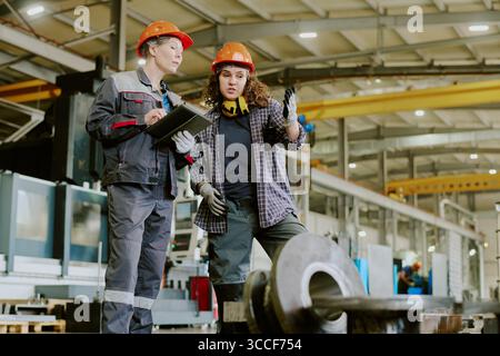Two Caucasian Women Engineers Discussing Industrial Machinery in Factory Stock Photo
