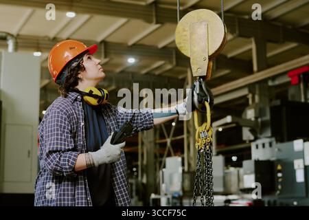 Young Adult Caucasian Woman Operating Overhead Hoist in Industrial Workshop Stock Photo