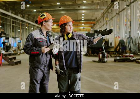 Two Young Adult Caucasian Women Collaborating in Industrial Factory Setting Stock Photo