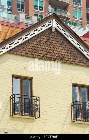 A yellow brick building in Yorkville features brown shingle gables, white trim, and two iron balconies beneath narrow wooden-framed windows. Stock Photo