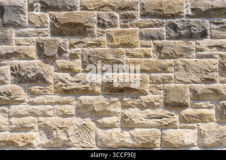 A close-up view of a textured beige stone wall with irregular rectangular blocks fitted together in a dry stack pattern. Stock Photo