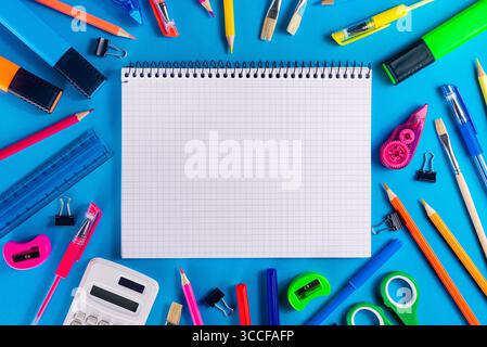 Top view of colorful school supplies surrounding a squared spiral notebook in the center on a bright blue background. Perfect for educational banners Stock Photo