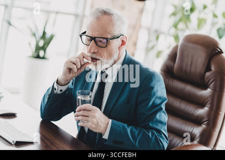 Mature businessman taking medication at work in his modern office environment during a busy workday Stock Photo