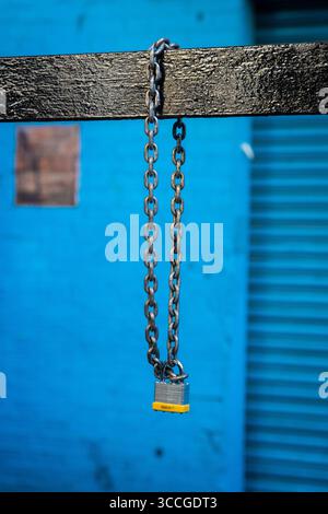 padlock hanging from a chain on a vivid blue background Stock Photo
