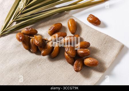 Organic dates arranged with palm leaves on a natural linen cloth over a white background, showing their golden-brown tones and fresh texture. Perfect Stock Photo