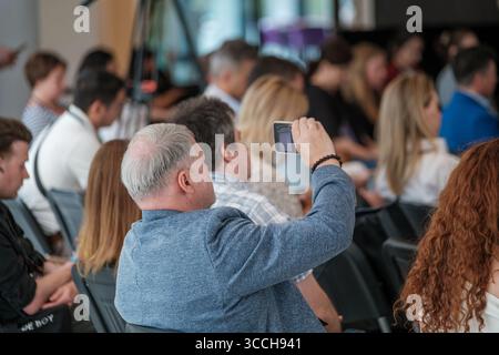 Audience member using smartphone to record event in professional conference with people engaged Stock Photo